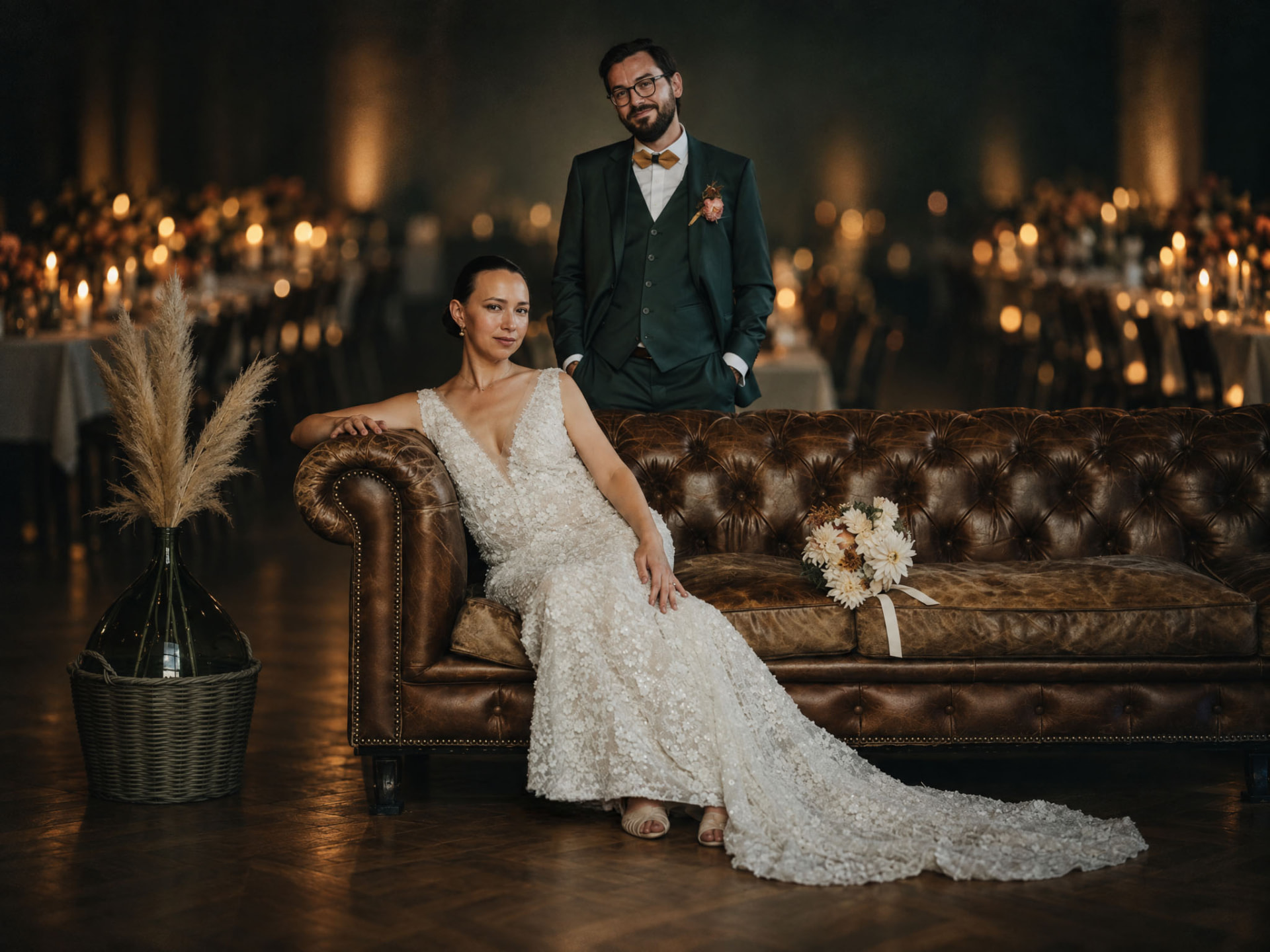 Portrait de mariage des mariés sur un canapé Chesterfield en cuir, dans une salle de réception éclairée aux bougies