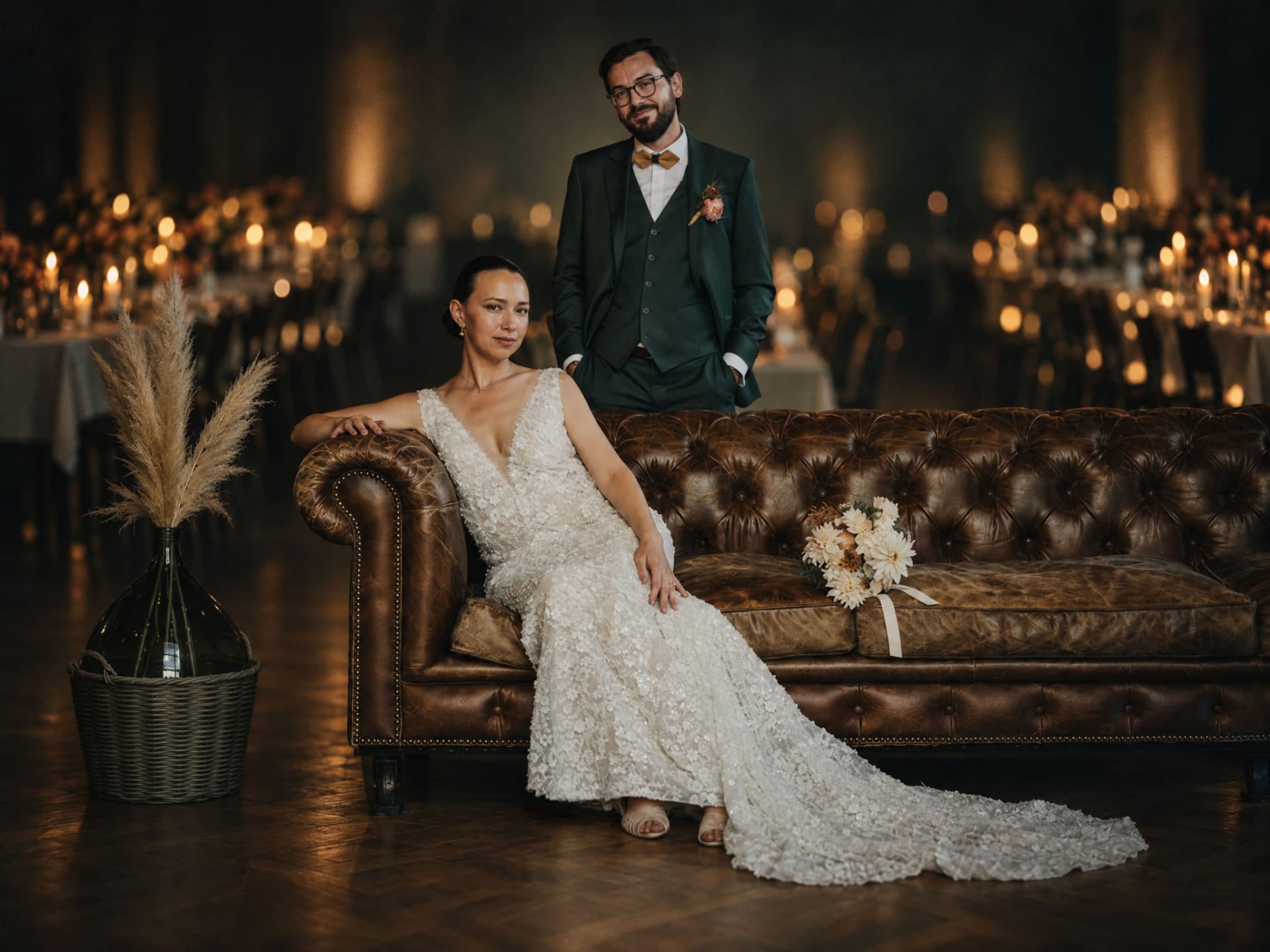 Portrait de mariage des mariés sur un canapé Chesterfield en cuir, dans une salle de réception éclairée aux bougies